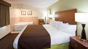 A hotel room with a large bed, a bedside table, a chair, a desk, a lamp, and a bathroom with a bathtub and towel rack. - AmericInn by Wyndham Hawley (Hawley)