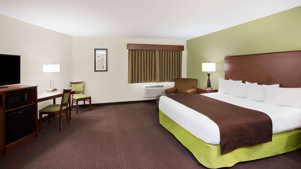 Una habitación de hotel con una cama grande, un escritorio con silla, un televisor y una ventana con cortinas.