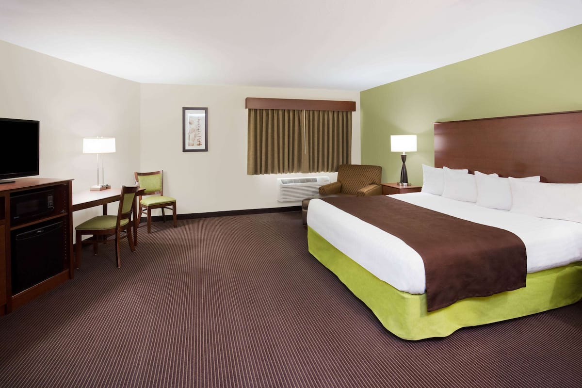 Una habitación de hotel con una cama grande, un escritorio con silla, un televisor y una ventana con cortinas.