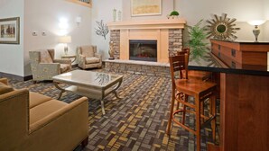 A living room with a fireplace, patterned carpet, and a dining area with a table and chairs. - AmericInn by Wyndham Hawley (Hawley)