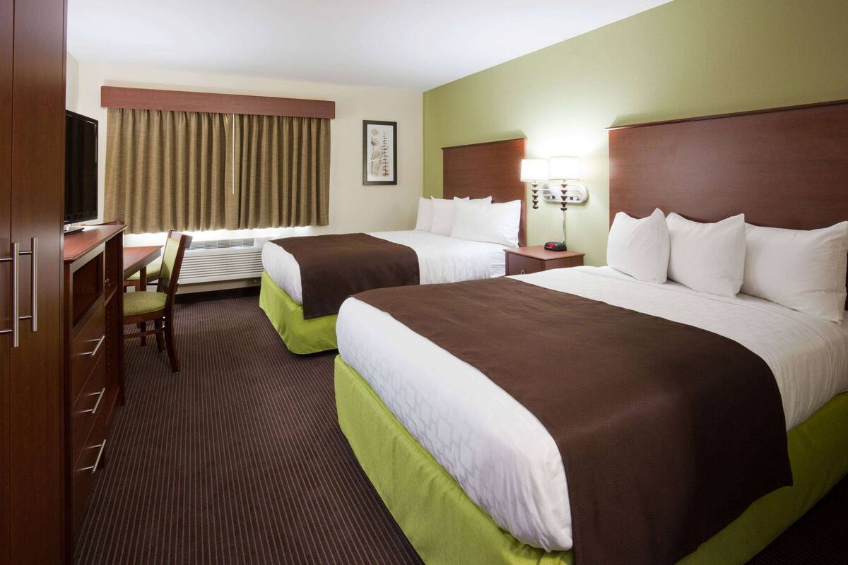 Habitación de hotel con dos camas, un escritorio, una silla, un televisor y un ventanal con cortinas.