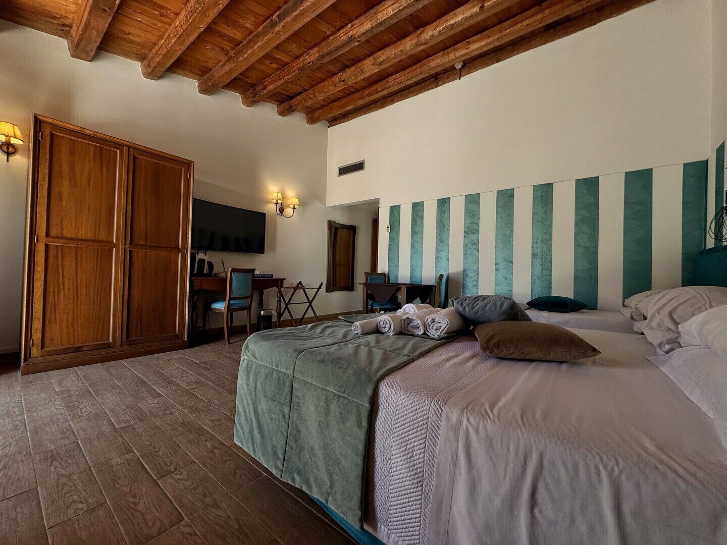 Ein Schlafzimmer mit Holzbalkendecke, einem Bett mit Kissen, einem Schreibtisch mit Stuhl und einem Kleiderschrank.