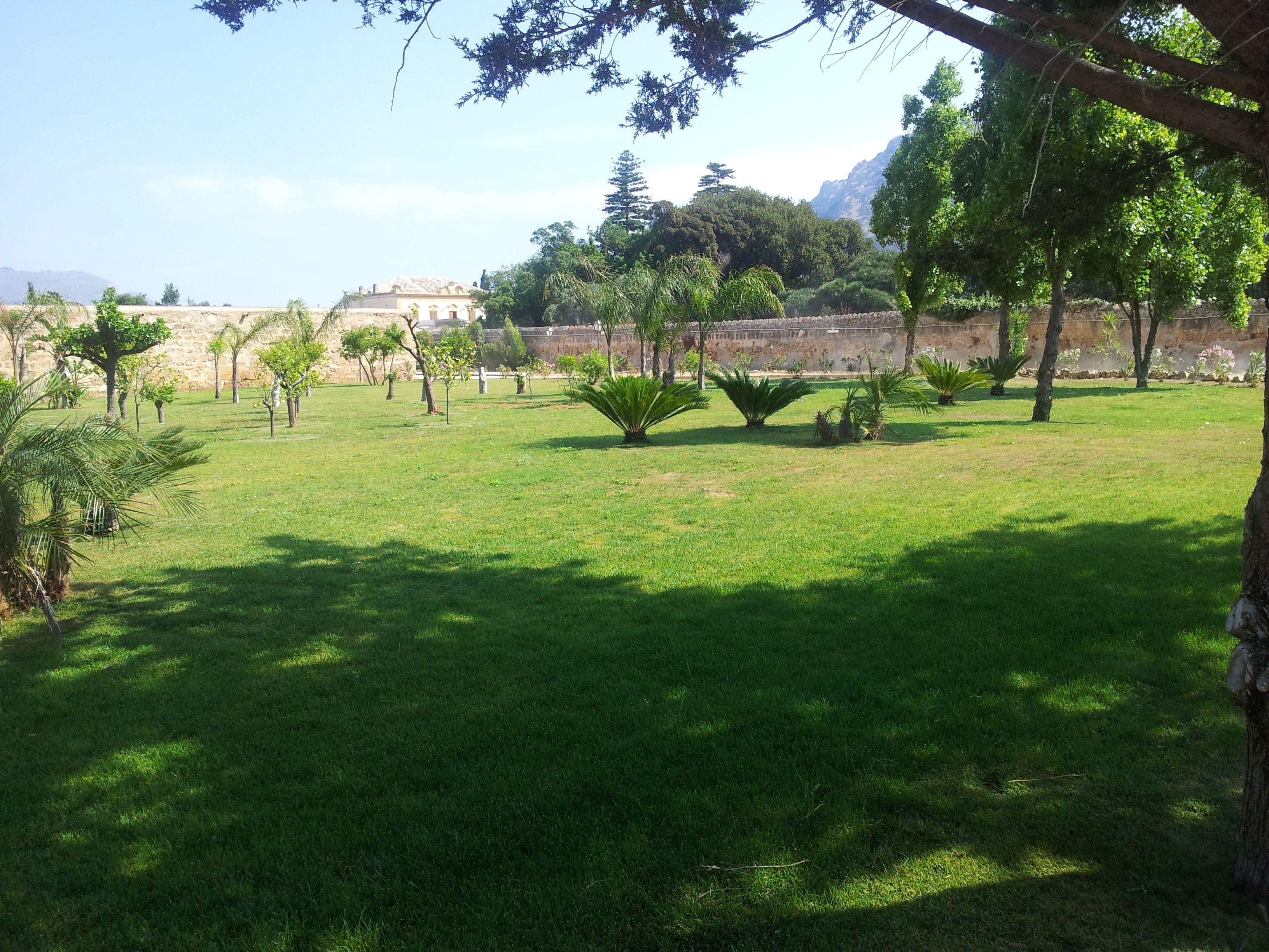 Um parque com gramado, árvores e um muro de pedra ao fundo.