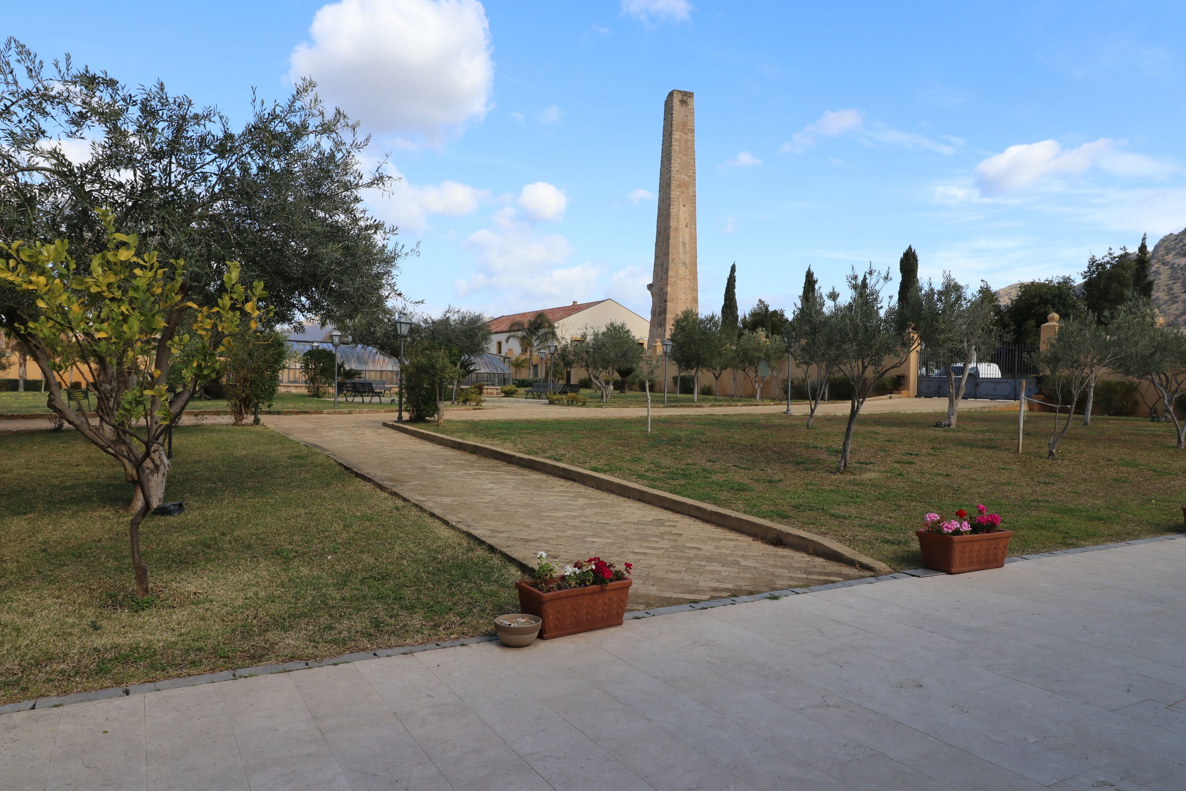 Une cour avec un monument imposant, un sentier et des plantes en pot.