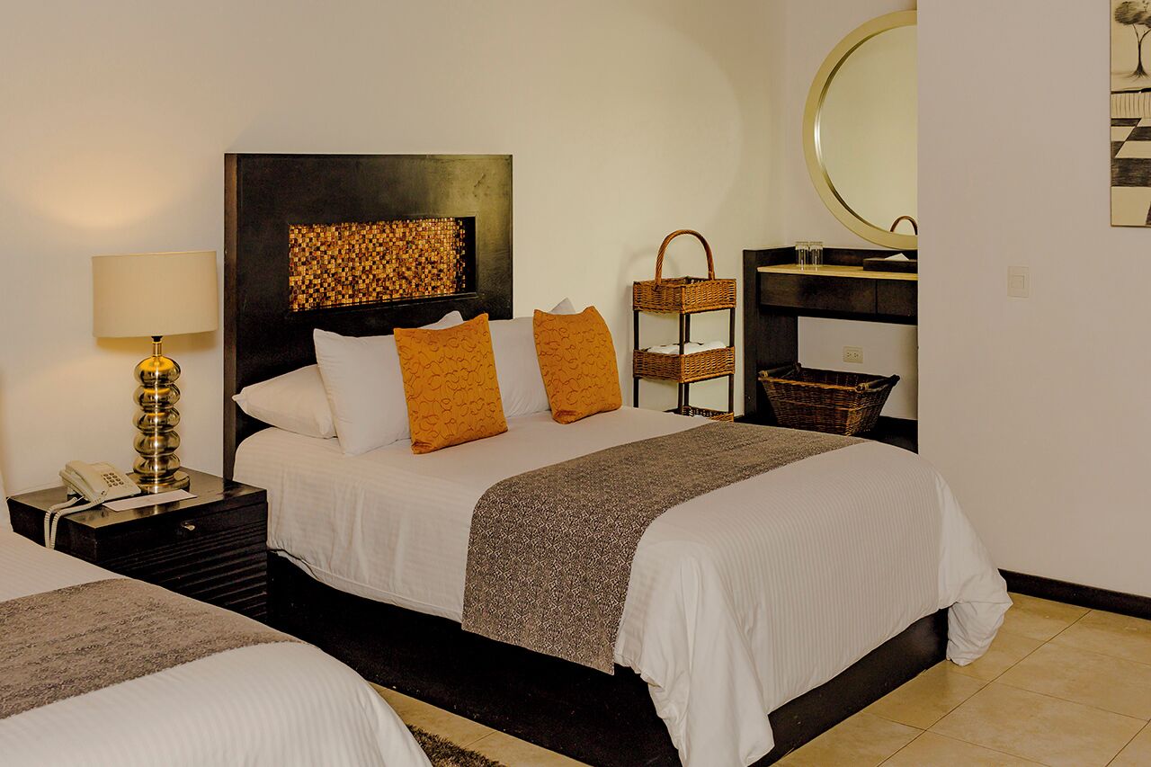 A hotel room with a large bed, a bedside table with a lamp, a mirror, and a wall-mounted artwork.