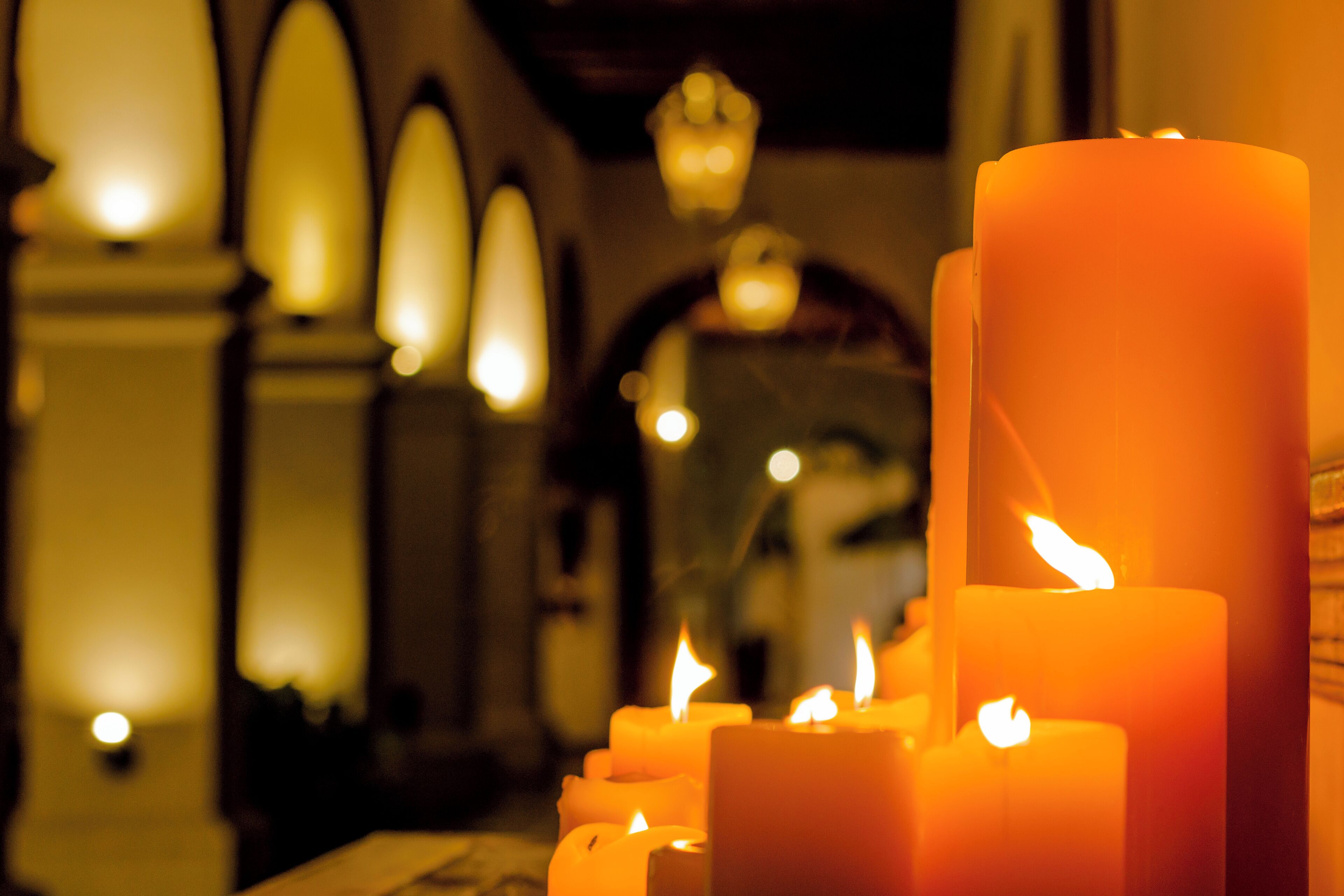 A row of lit candles in a dimly lit room with arched ceilings and hanging lights.