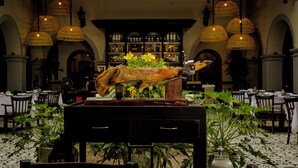 A restaurant with a central display of a roasted pig, surrounded by tables and chairs, with hanging lamps and a bar in the background. - Hotel Boutique Hacienda Guadalupe (San Miguel de Allende)
