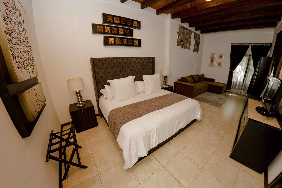Un dormitorio con una cama grande, una mesita de noche, una silla, un sofá y una televisión.