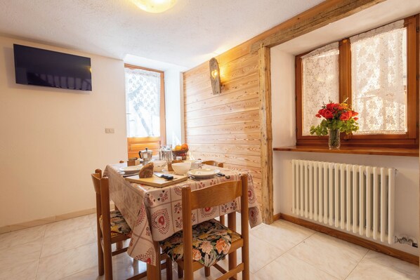Un comedor con una mesa preparada para dos personas, una silla de madera, un radiador y una ventana con cortinas de encaje.
