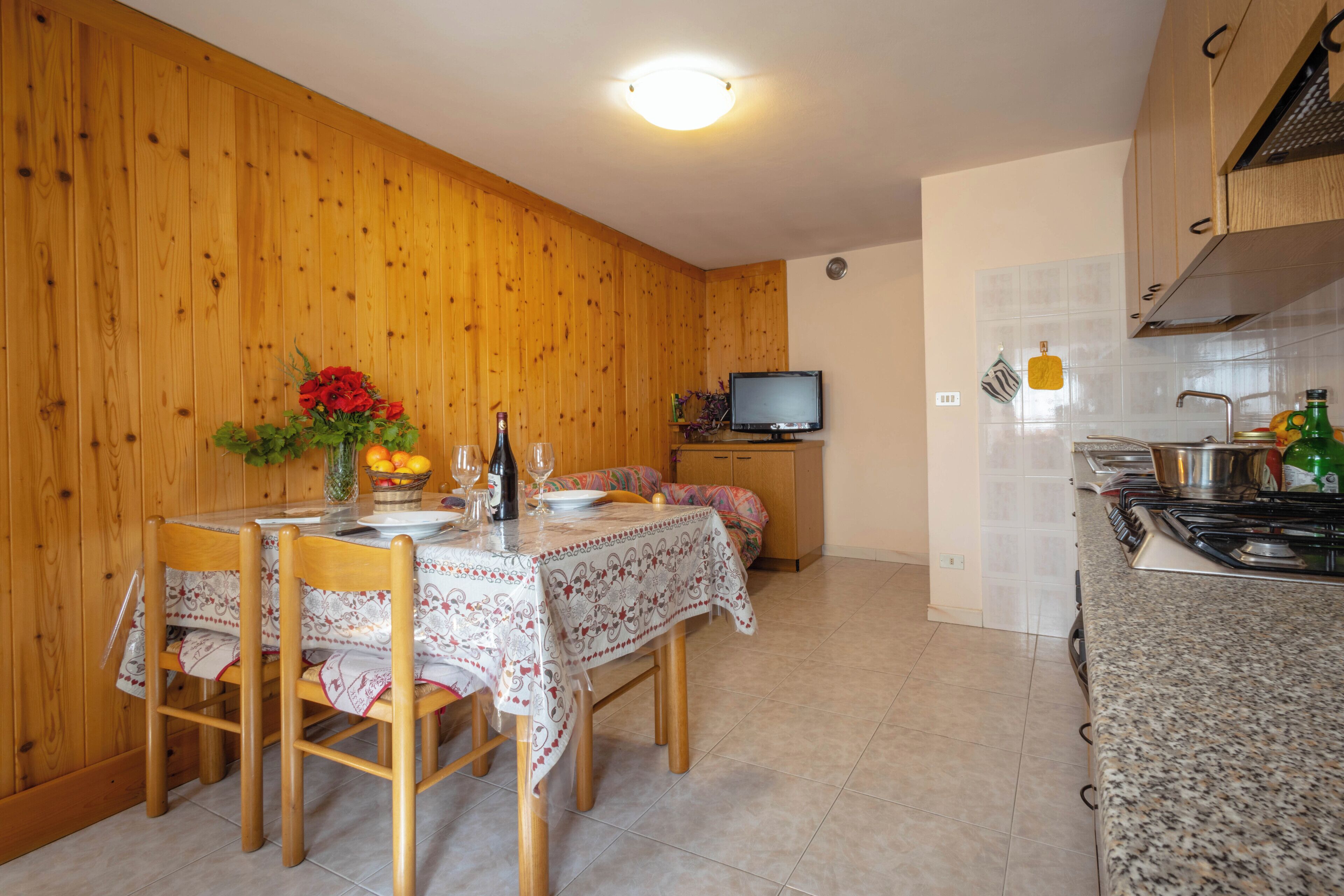 A wooden-paneled room with a dining table set for four, a television, and a kitchen area with a stove.