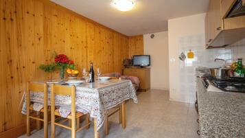 A wooden-paneled room with a dining table set for four, a television, and a kitchen area with a stove.