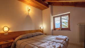 A bedroom with a wooden headboard, a large bed with a beige quilt, two bedside lamps, and a window with a view of the outdoors. - Le Vieux Noyer (Saint-Pierre)