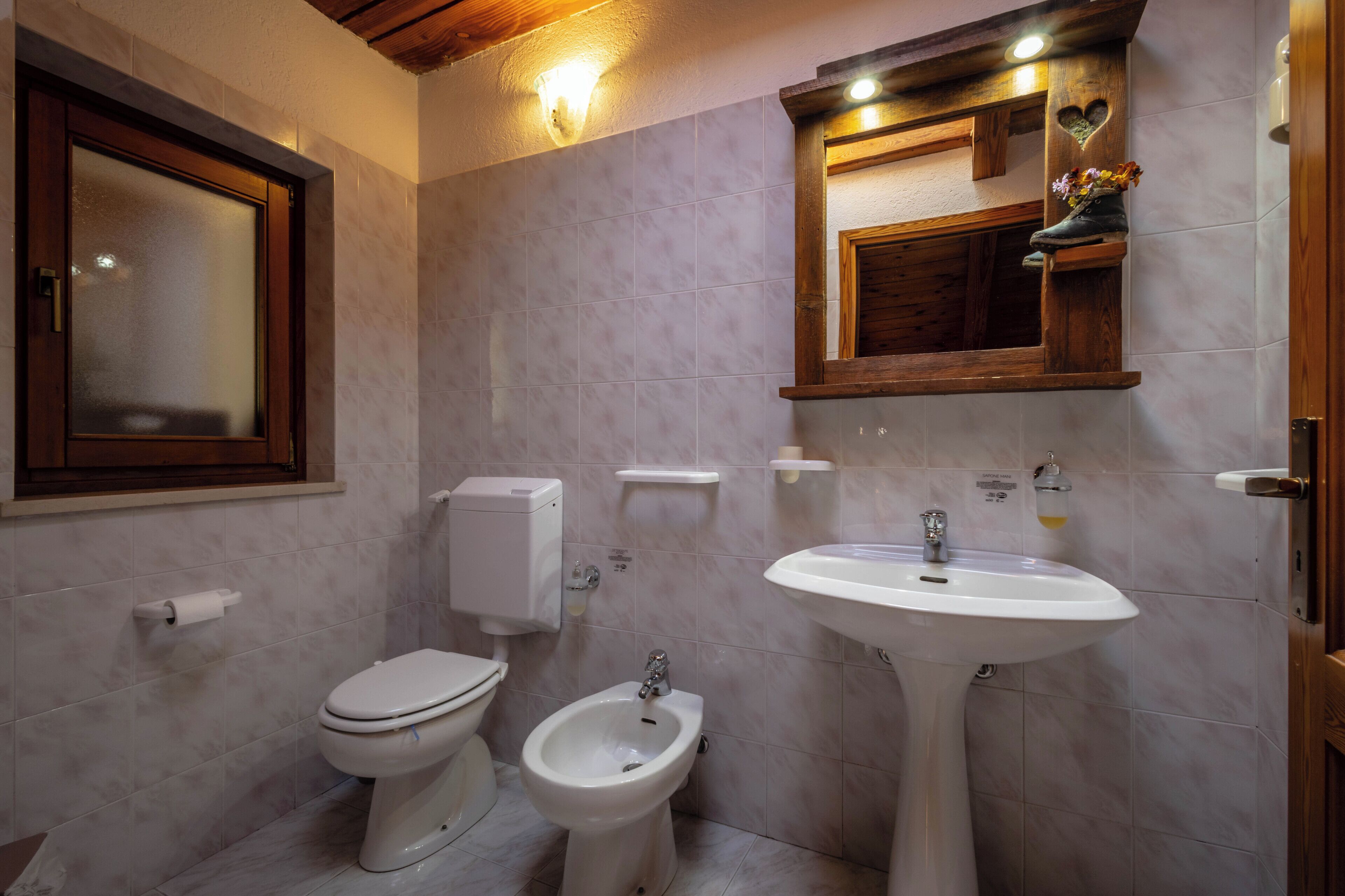 Un baño con inodoro, bidé y lavabo, tocador de madera y un espejo con un adorno con forma de corazón.