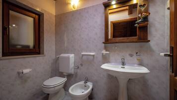 Un baño con inodoro, bidé y lavabo, tocador de madera y un espejo con un adorno con forma de corazón.