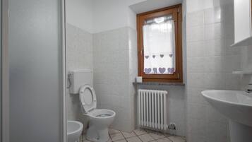 Un baño pequeño con inodoro, ventana y cortina con estampado de corazón, y un radiador.