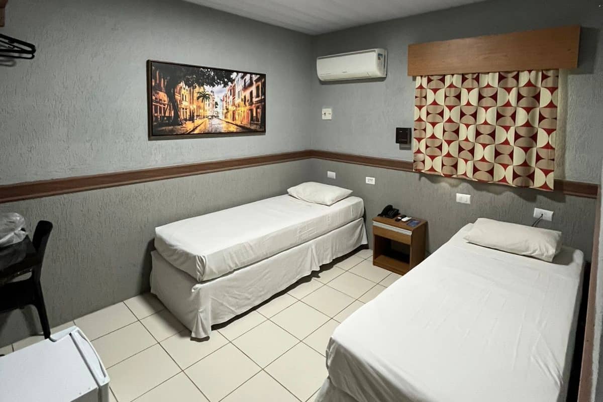 A hotel room with two single beds, a desk, a chair, and a picture on the wall.