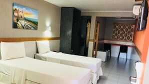 A hotel room with two single beds, a painting of a coastal scene, a kitchenette, and a TV. - Inter Hotel (Recife)