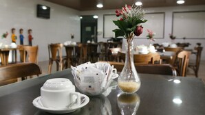 A dining table with a white teapot, a cup, a sugar bowl, and a vase with flowers. - Inter Hotel (Recife)