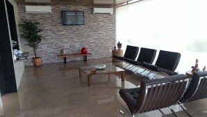 A modern waiting area with a stone wall, a flat-screen TV, a coffee table, and a seating area with black chairs. - Inter Hotel (Recife)