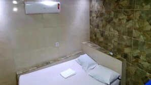 Hotelkamer met een bed, witte lakens, een wandairconditioner en een muur met een stenen patroon.