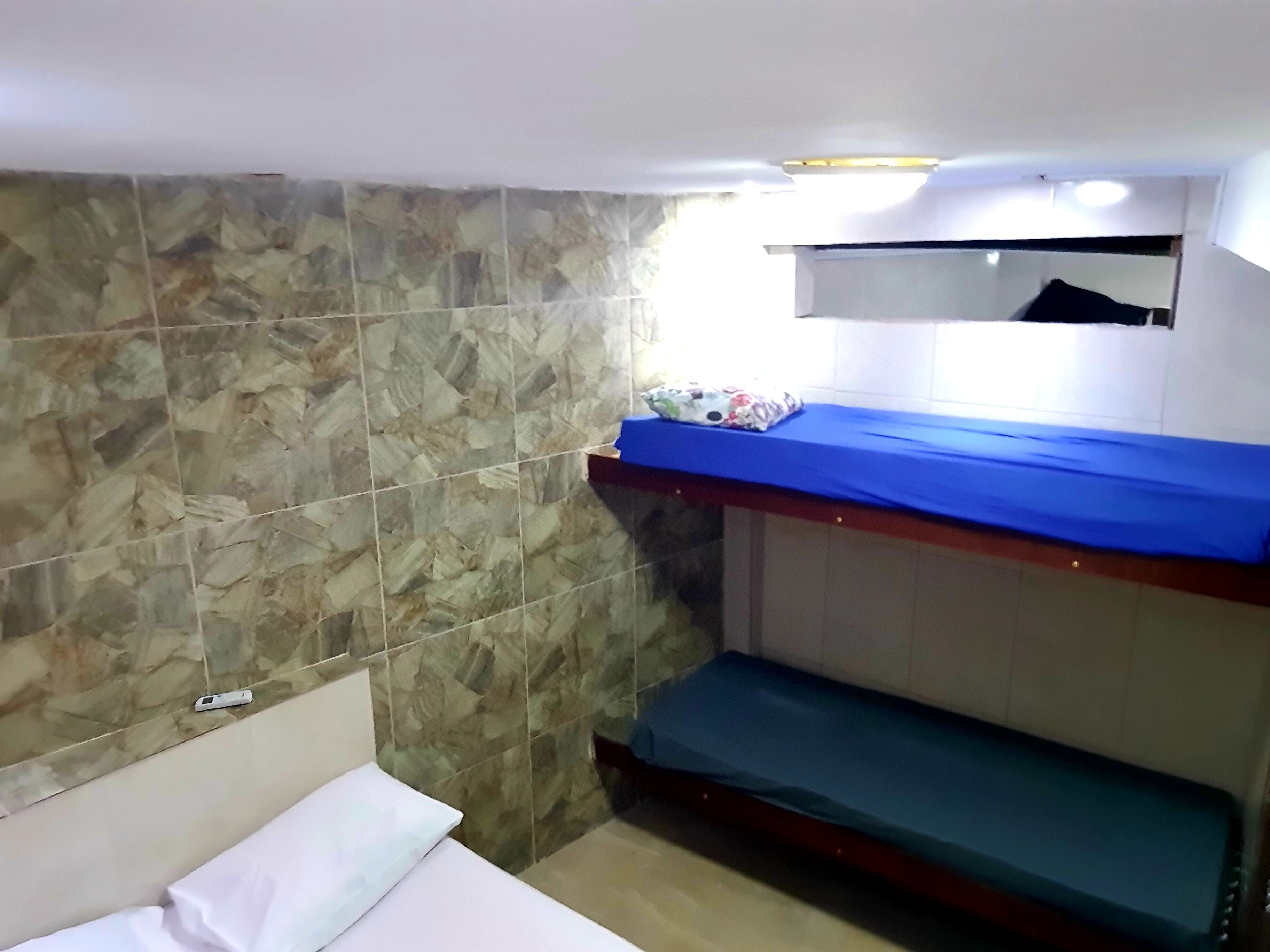 A small, compact room with a bunk bed, a single bed, and a tiled wall.