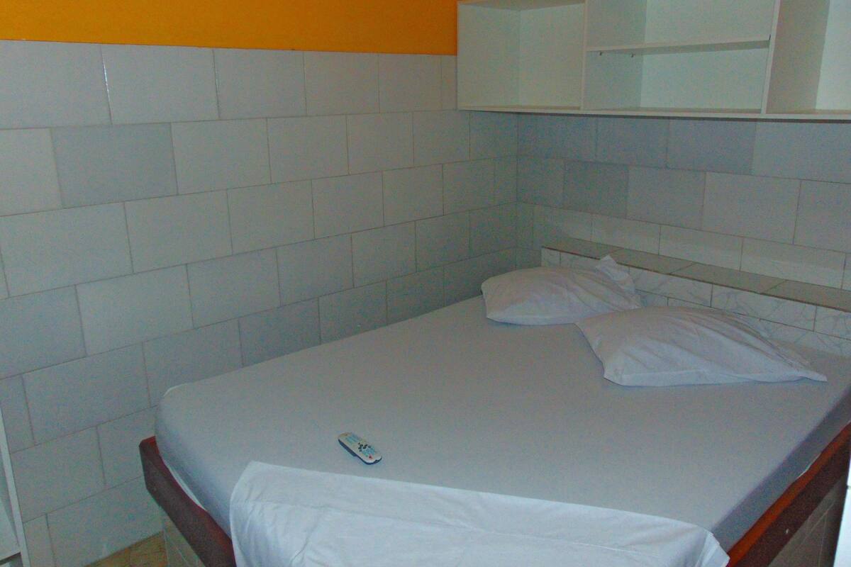 Ein Einzelbett mit weißer Bettwäsche, eine Fernbedienung auf dem Bett und ein weißes Kopfteil.