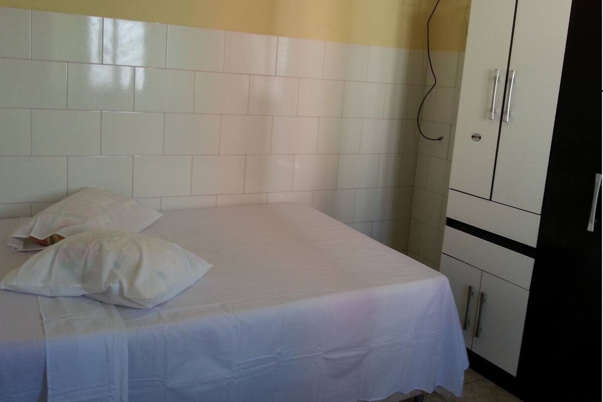 Ein Einzelbett mit weißer Bettwäsche in einem Zimmer mit weißen Fliesenwänden und einem weißen Schrank.