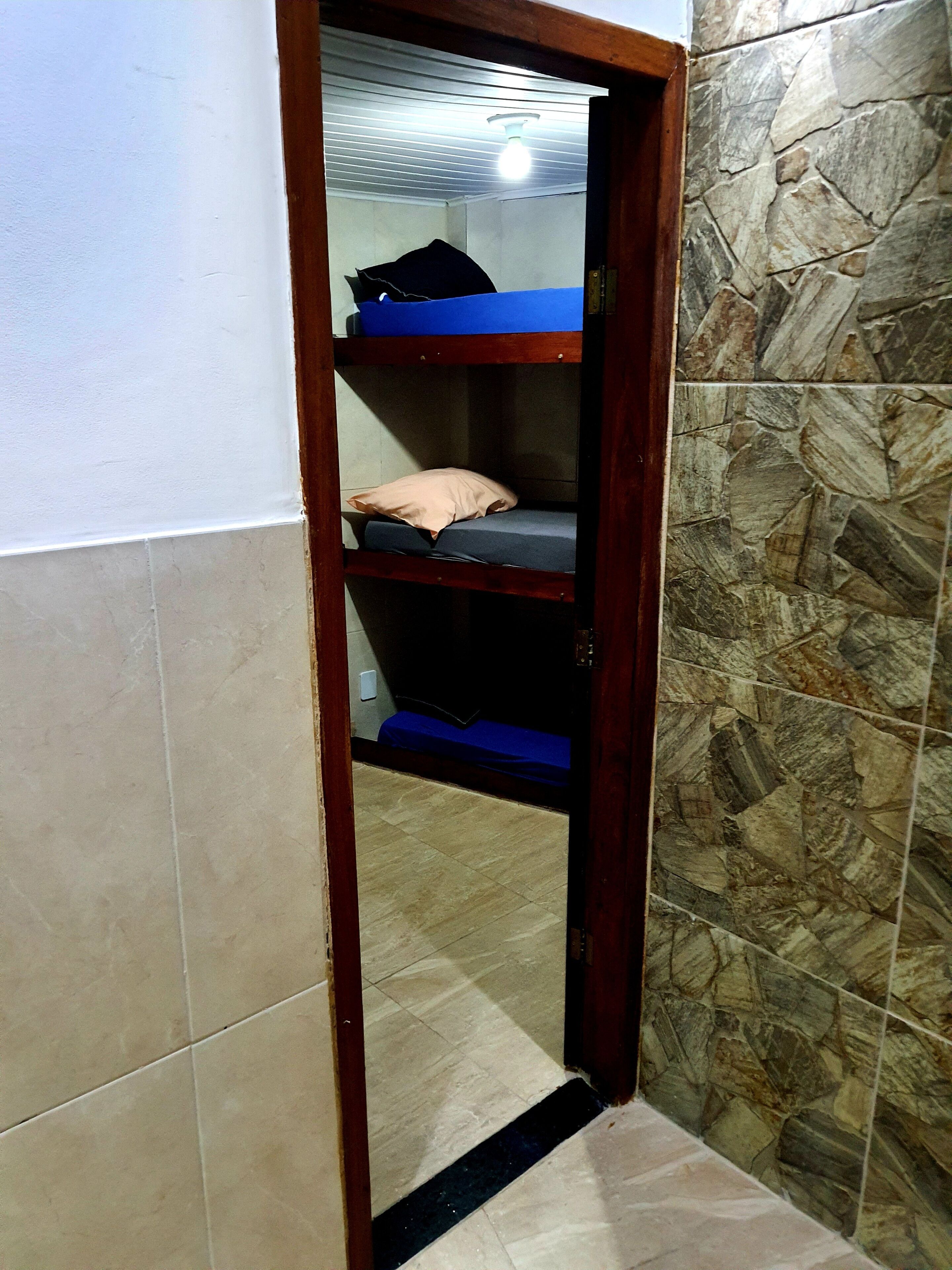 A narrow doorway leading to a room with a bunk bed, a ceiling light, and a stone-patterned wall.
