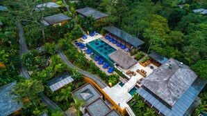 An aerial view of a resort with multiple bungalow-style accommodations, a central pool area with lounge chairs, and a well-maintained garden. - Nayara Springs - Adults only (La Fortuna)