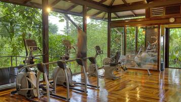 Une salle de sport équipée de divers appareils d’exercice, dotée de grandes fenêtres et d’un plancher en bois.