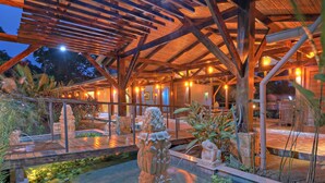 A wooden pergola structure with a stone fountain and decorative sculptures in a landscaped garden area. - Nayara Springs - Adults only (La Fortuna)