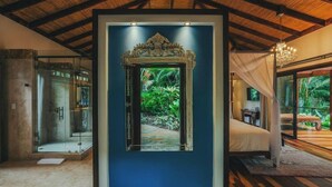 A room with a large mirror, a bed, a glass shower, and a view of greenery. - Nayara Springs - Adults only (La Fortuna)