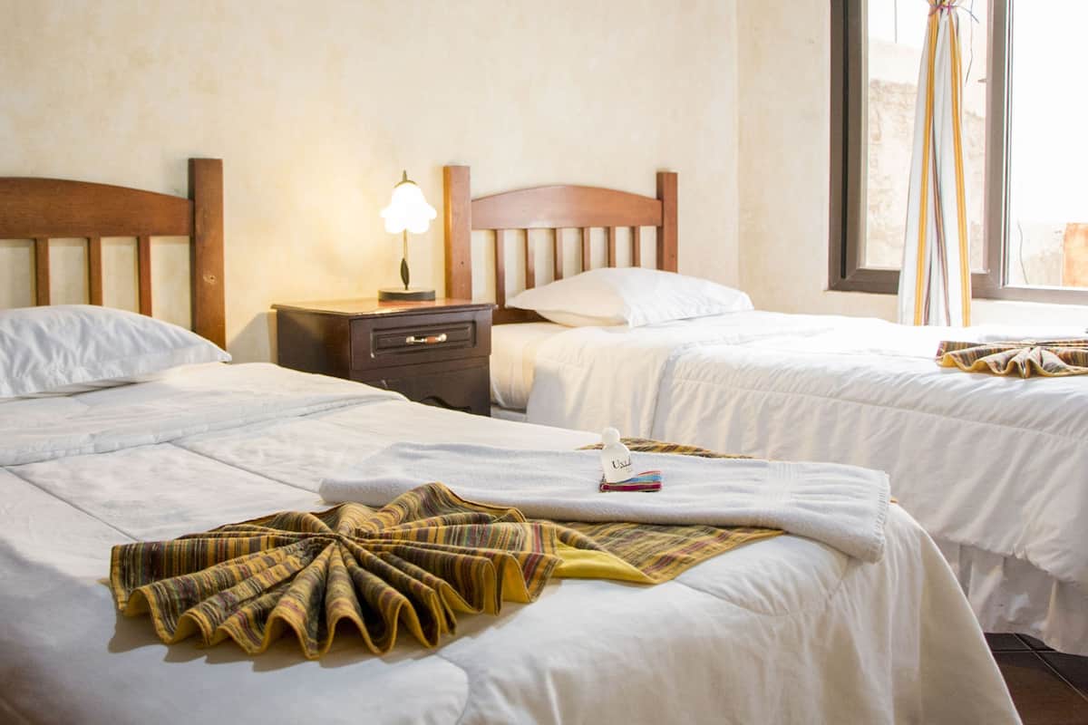 Une chambre d’hôtel avec deux lits, une table de chevet avec une lampe et une fenêtre avec des rideaux.