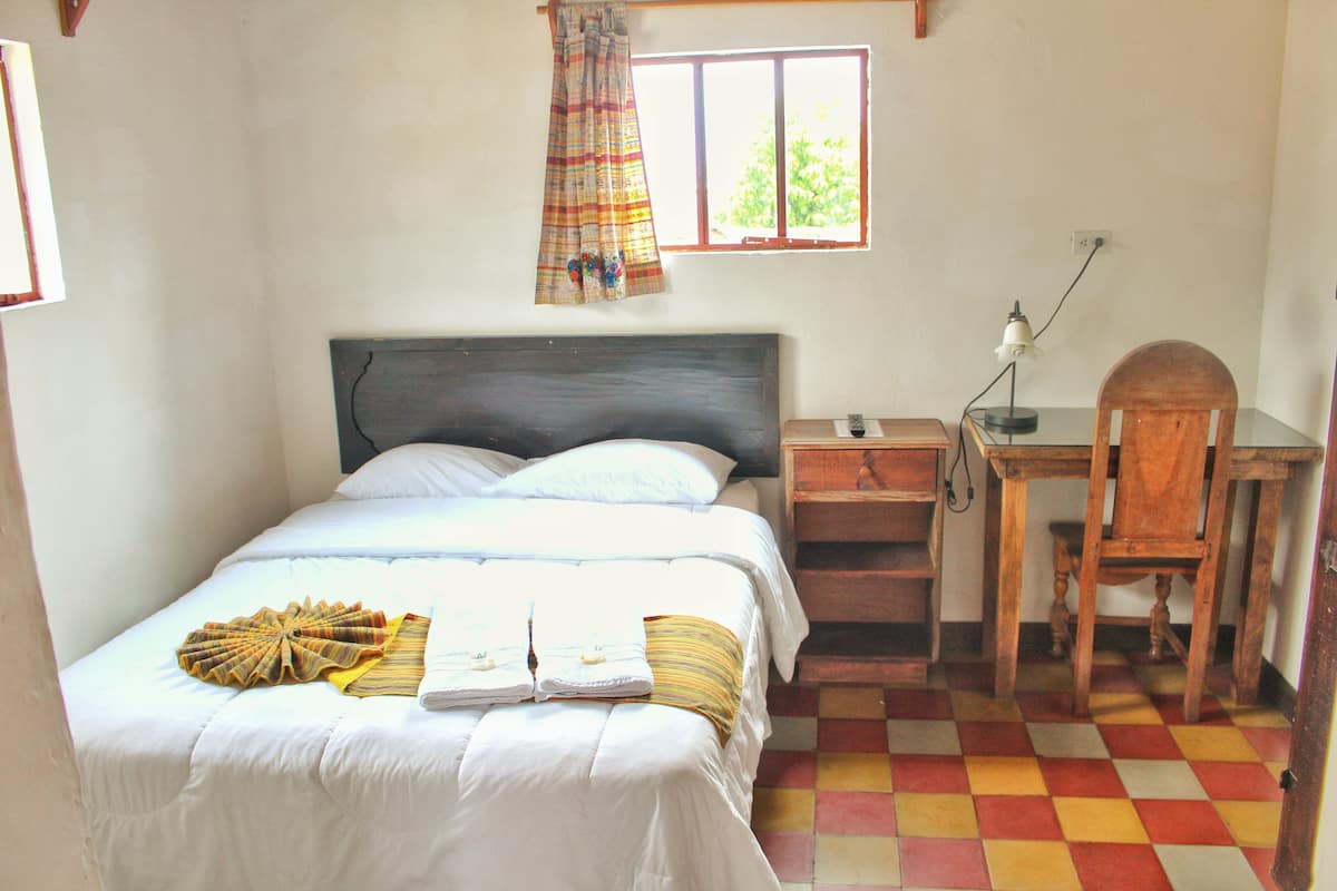 Une chambre à coucher avec un lit, un bureau, une chaise et une fenêtre avec des rideaux.