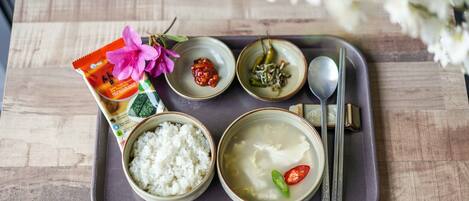 A tray with a package of rice, a bowl of rice, a bowl of soup, a small bowl of chili, and a spoon.