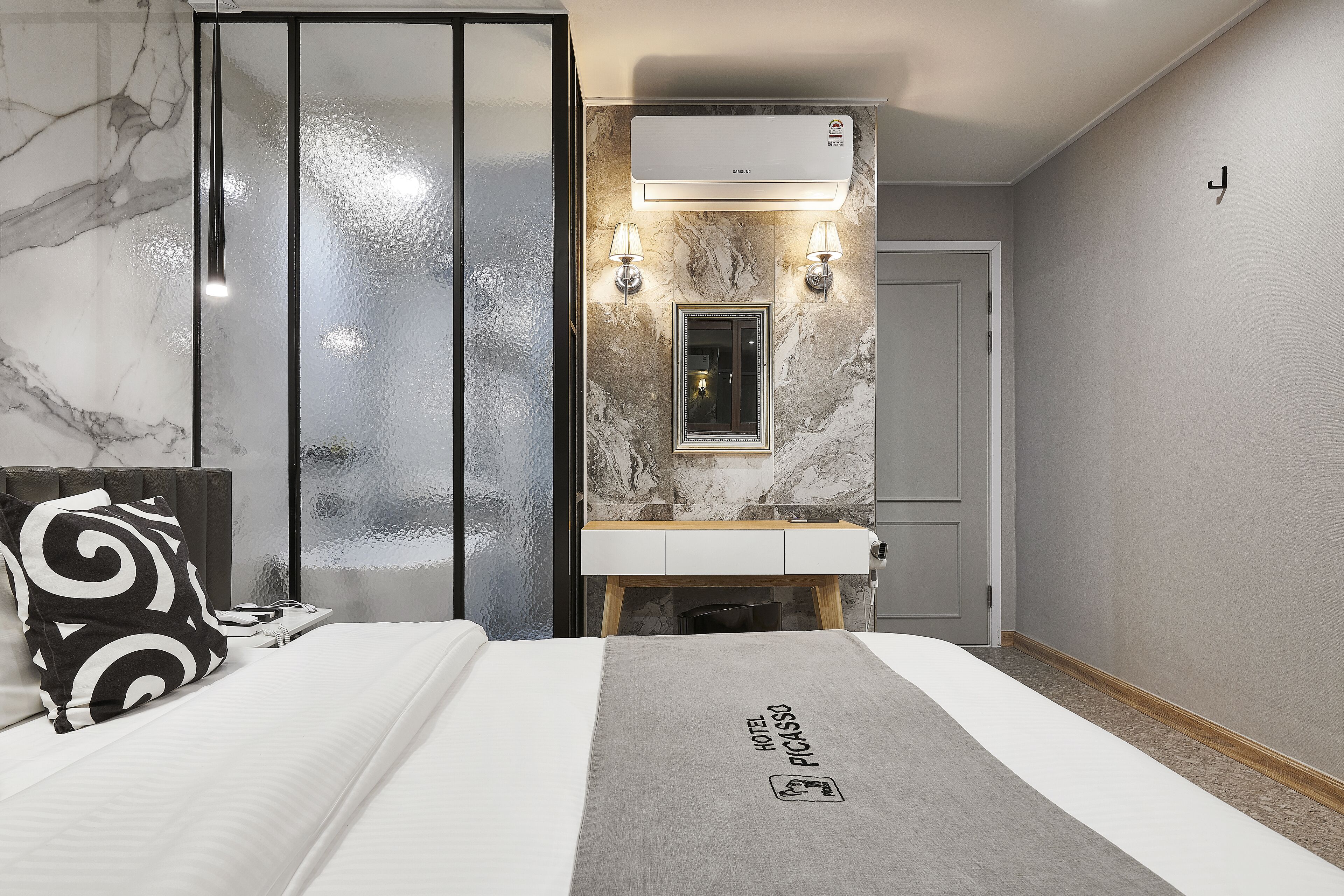 A hotel room with a bed, a marble-patterned wall, an air conditioning unit, and a mirror above the sink.