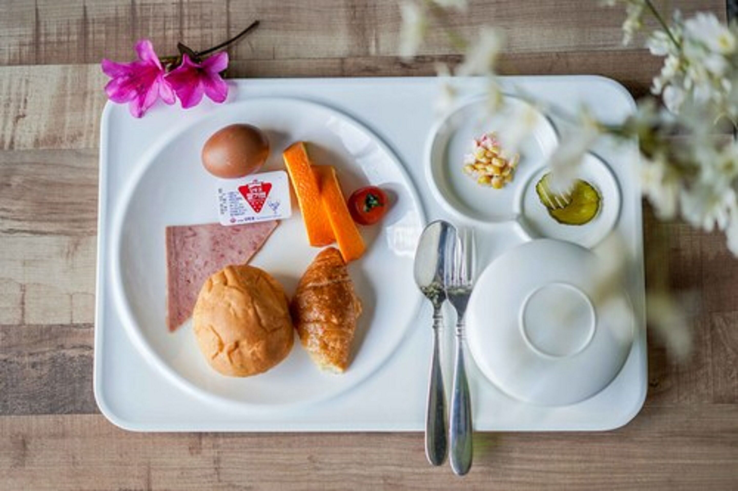 Una bandeja con alimentos como un croissant, un sándwich de jamón, un huevo cocido, una rebanada de queso y encurtidos.