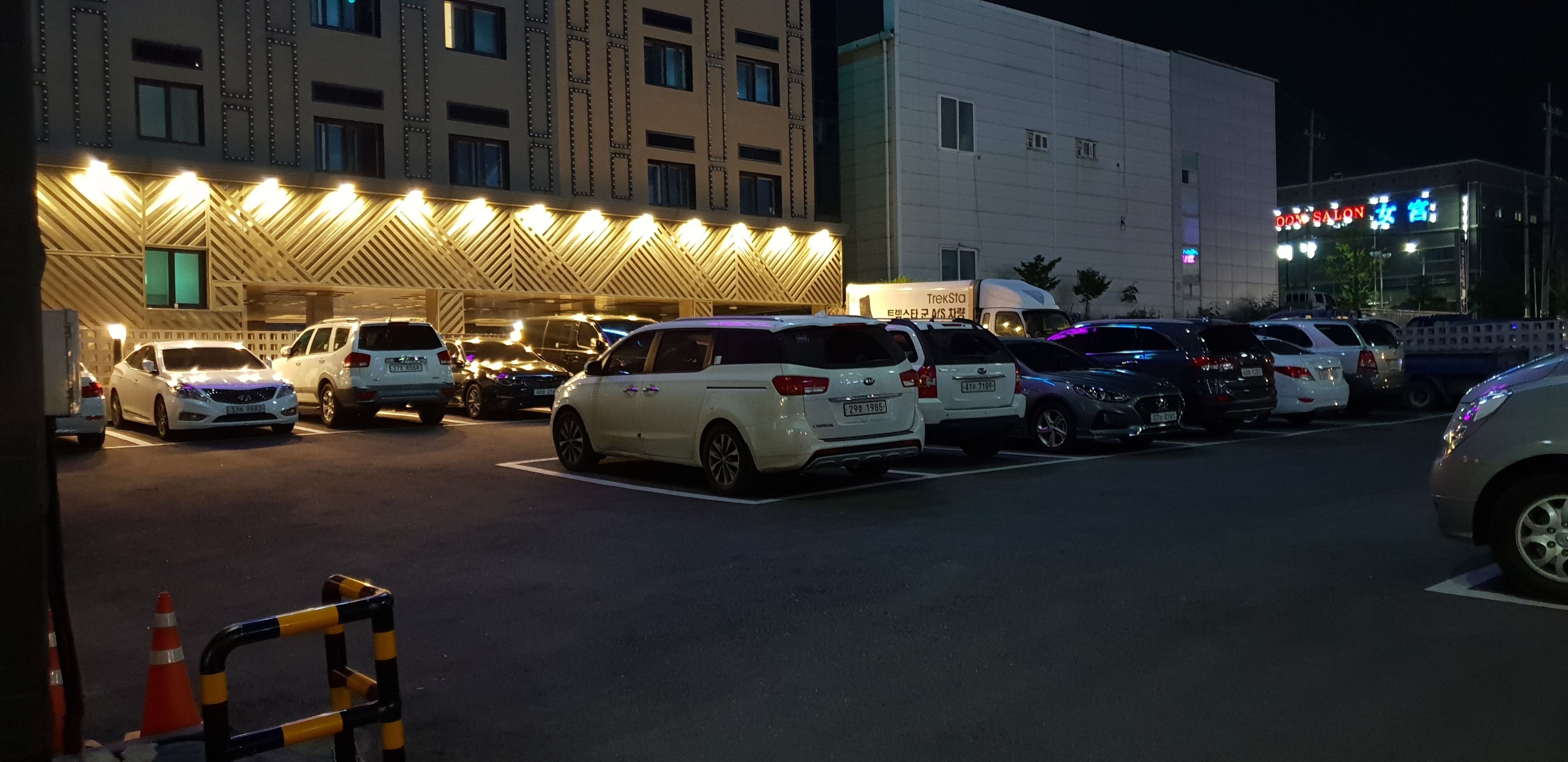 Un parcheggio con diverse auto parcheggiate di fronte a un edificio con insegne illuminate.