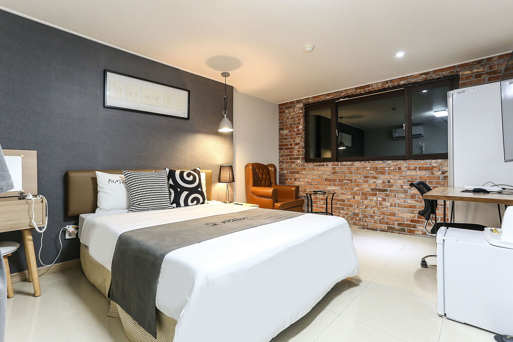 A hotel room with a large bed, a desk, a chair, a brick wall, and a window.
