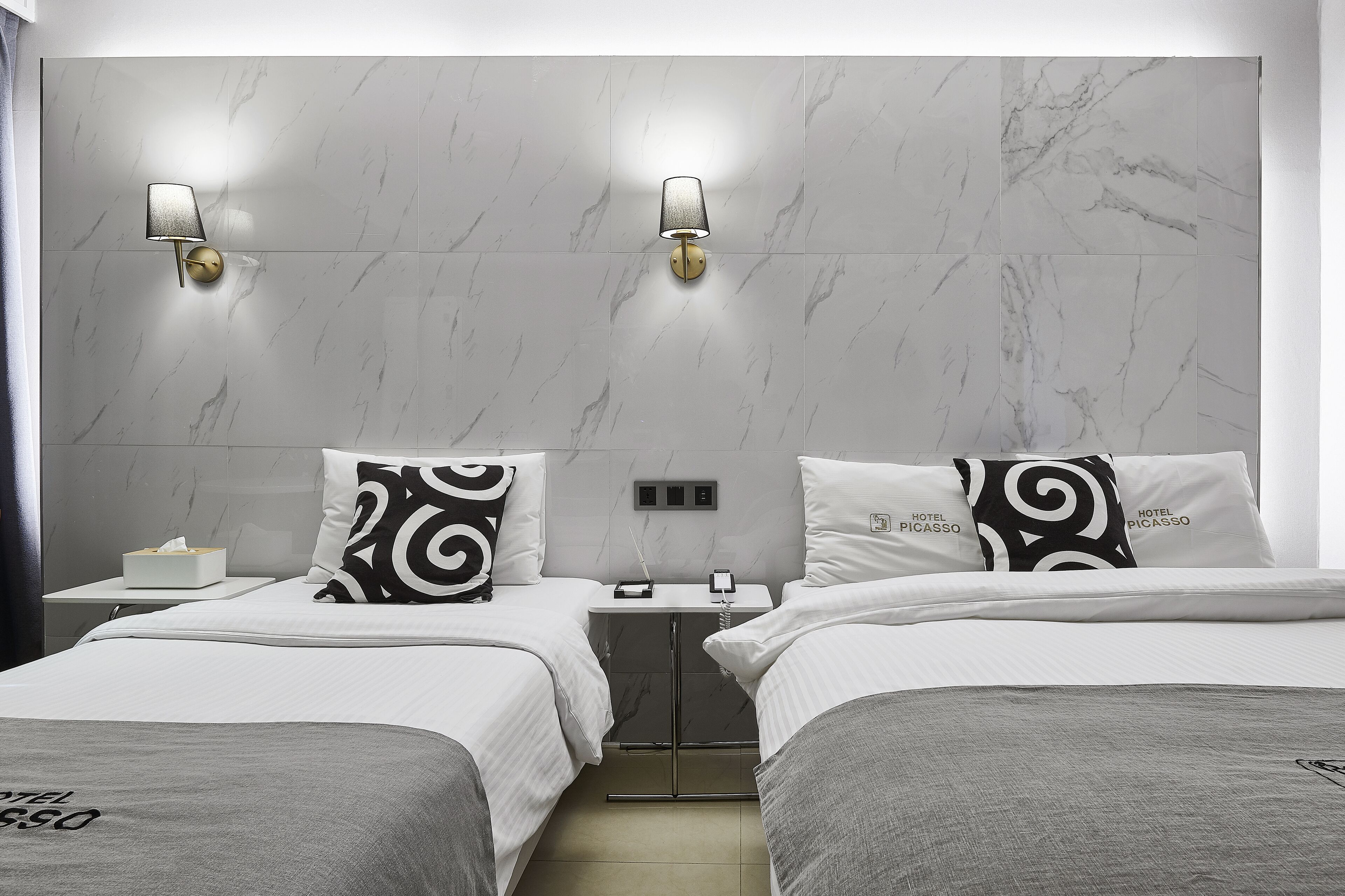 A hotel room with two beds, marble walls, and wall-mounted lamps.