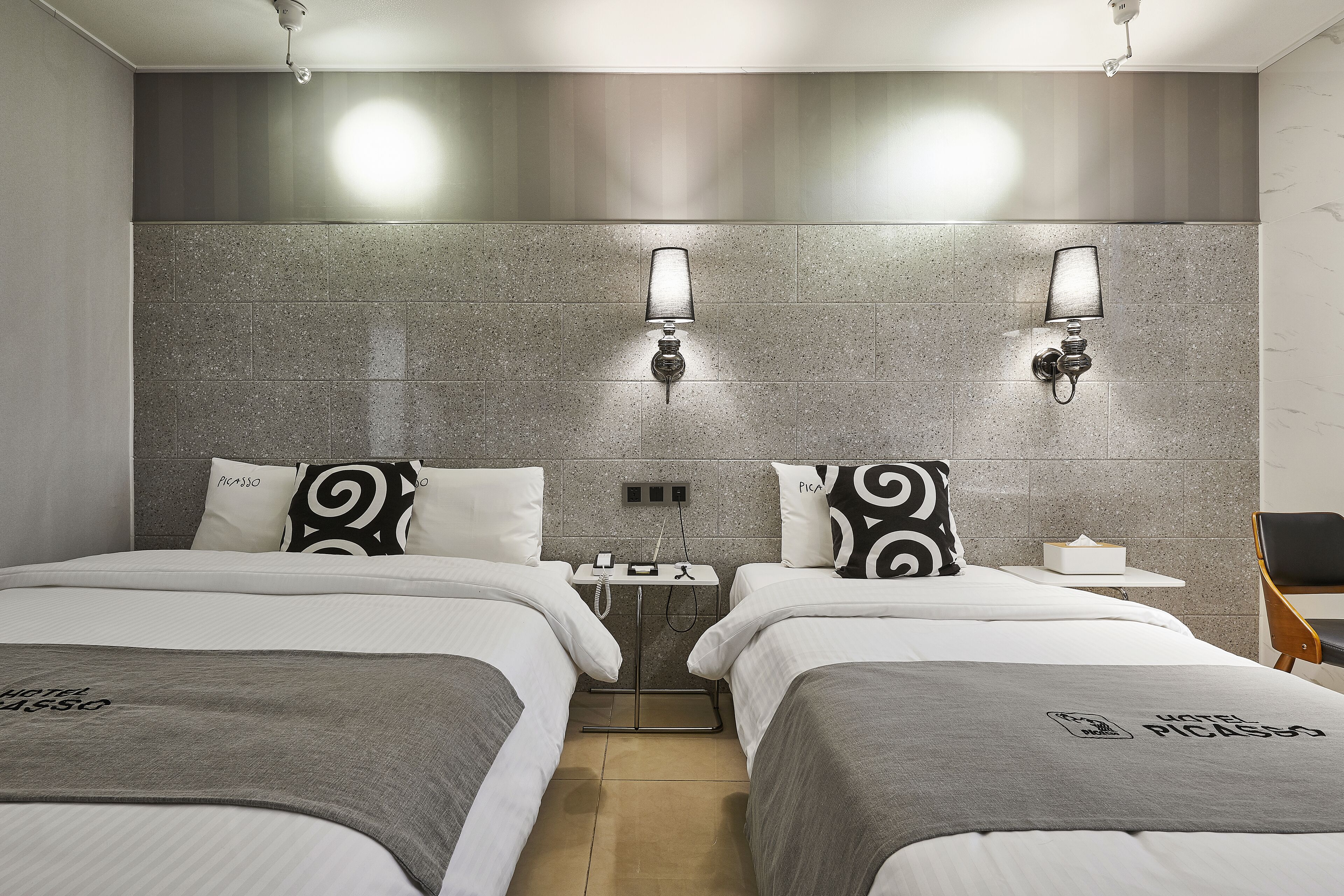 A hotel room with two beds, a nightstand, and a chair.