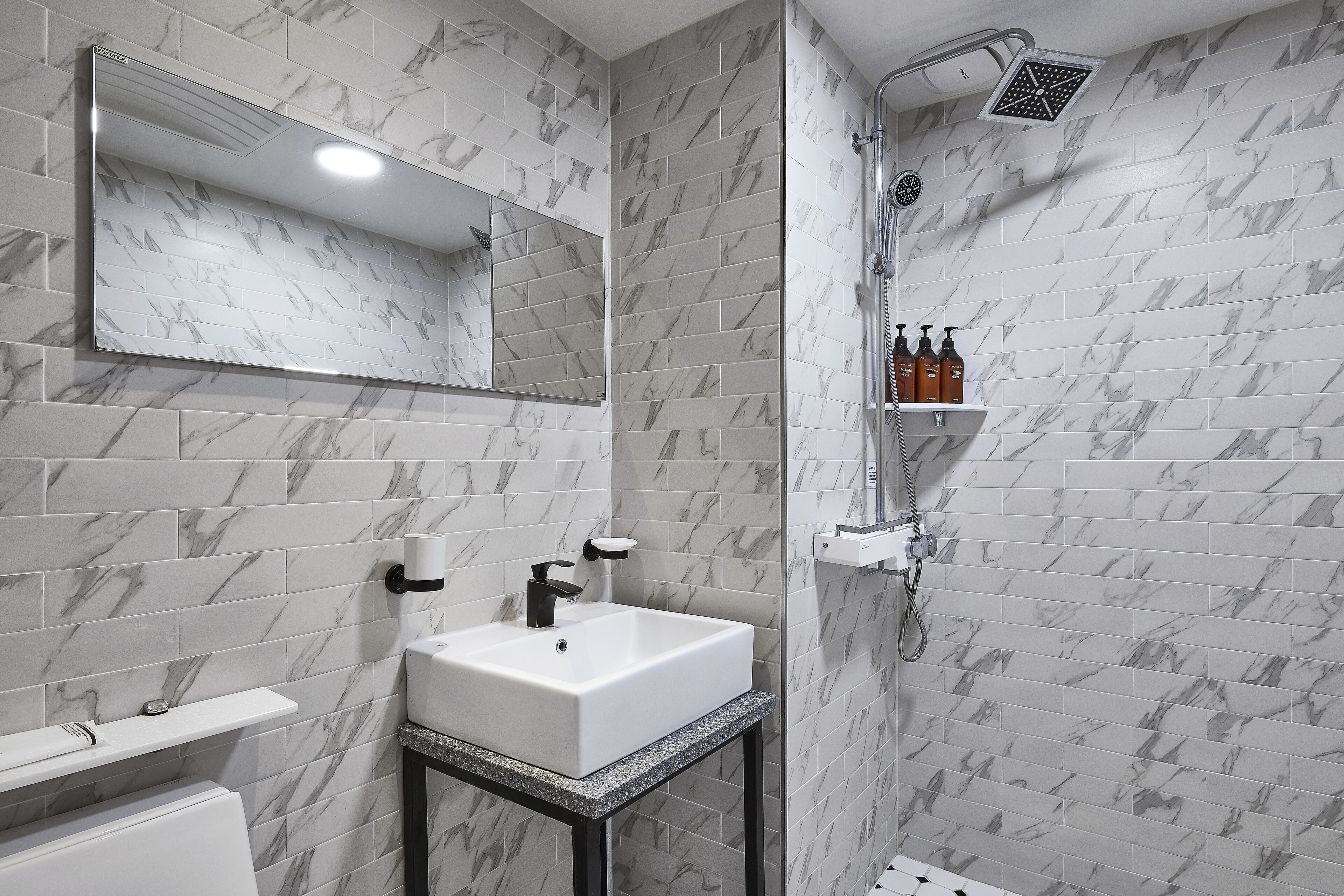 A bathroom with a white sink, a mirror, and a shower with a handheld showerhead.