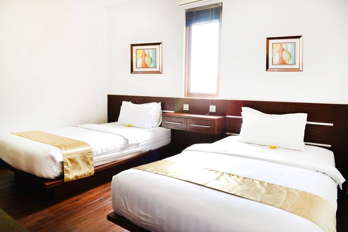A hotel room with two beds, wooden headboards, white bedding, and two framed abstract paintings on the walls.