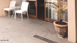 A modern hotel exterior with a glass door entrance, numbered 305, and a seating area with white chairs and a table. - Devata Suite & Residence (Legian)