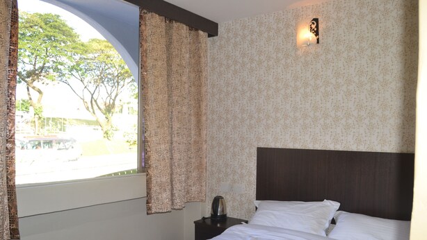 A hotel room with a large window, a bed with white linens, a dark headboard, and a nightstand with a kettle. - Cosmic Boutique (Kuala Lumpur)
