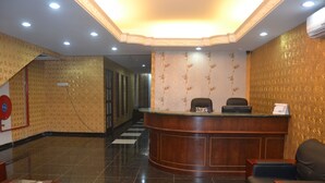 A hotel reception area with a curved wooden reception desk, two black chairs, a patterned carpet, and a tiled floor. - Cosmic Boutique (Kuala Lumpur)