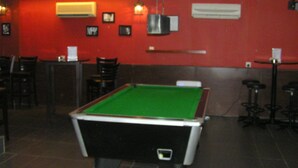 A billiards table in a room with red walls, a ceiling fan, and a bar area with stools. - Cosmic Boutique (Kuala Lumpur)