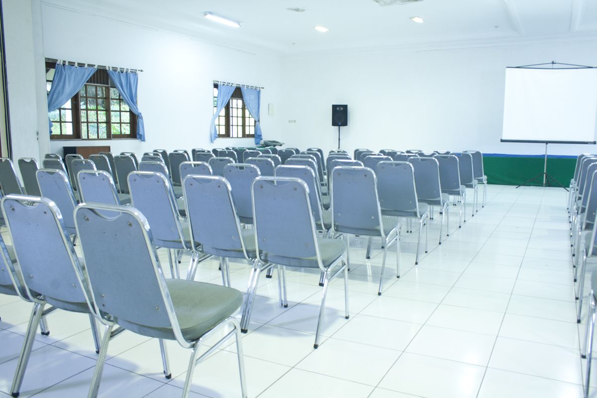 Un salón de conferencias con filas de sillas, una pizarra y una pantalla de proyector.