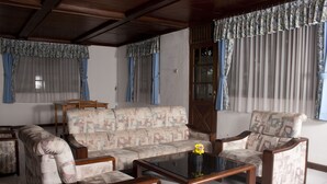 Una sala de estar con un sofá, dos sillones, una mesa de centro y cortinas en las ventanas.
