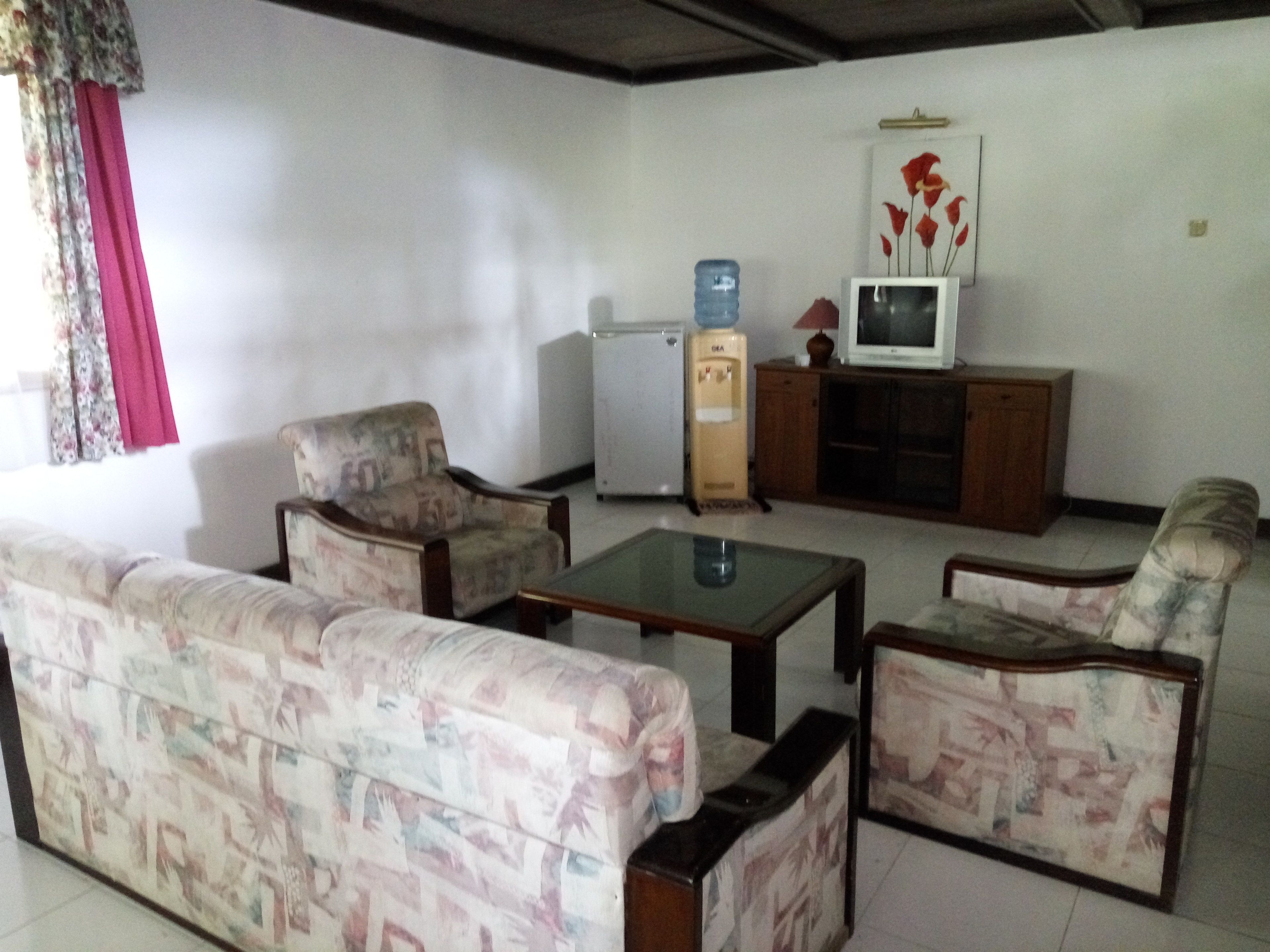 A living room with patterned sofas, a small table, a water dispenser, and a television on a wooden cabinet.